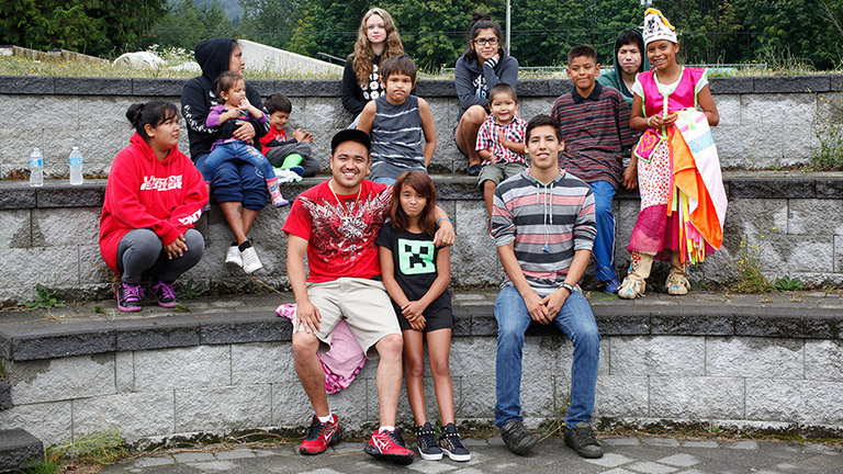 Youth, both male and female, are sitting outdoors on several rows of tiered stone seating.