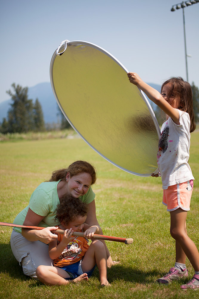 A mother and her two young children are playing outside on the grass and having their photo taken.