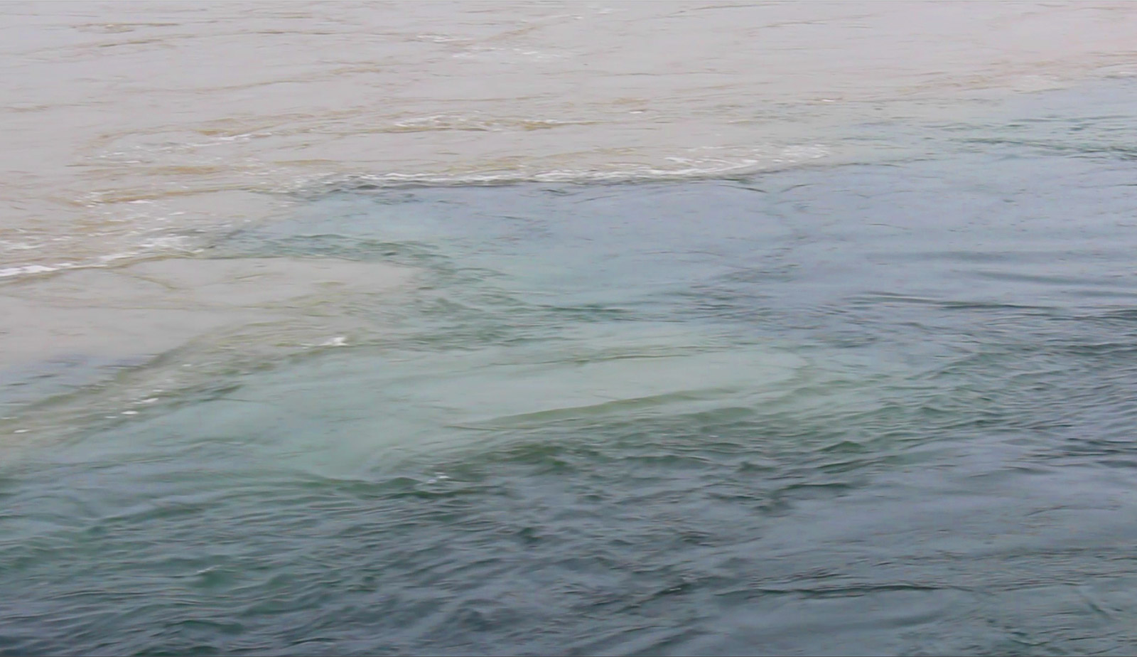 Image of one river, of greyish-brown colour, mixing with another river of blue-green colour. The two colours are separated, but a line down the middle shows where the colours are blending together.