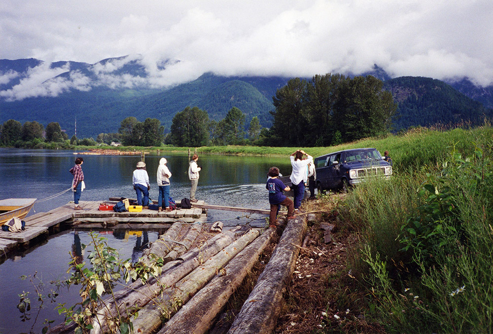 A group of field school students are standing on a wooden dock as they prepare to launch a boat into the river.