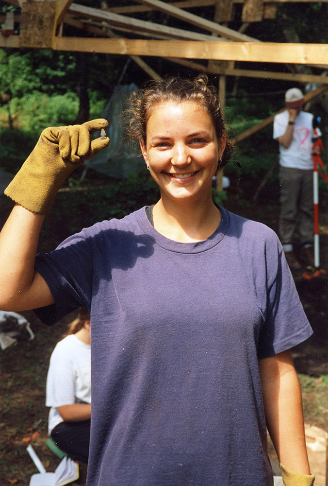 A field school student holds a tiny arrowhead in between her gloved fingers.
