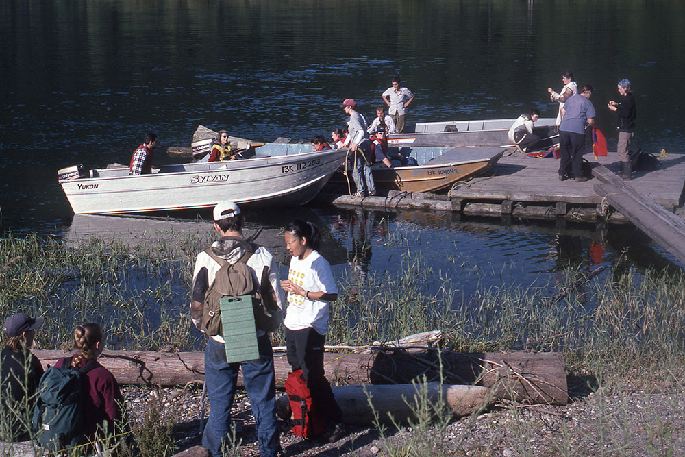 Students gather around a small wooden dock, loading supplies into boats.
