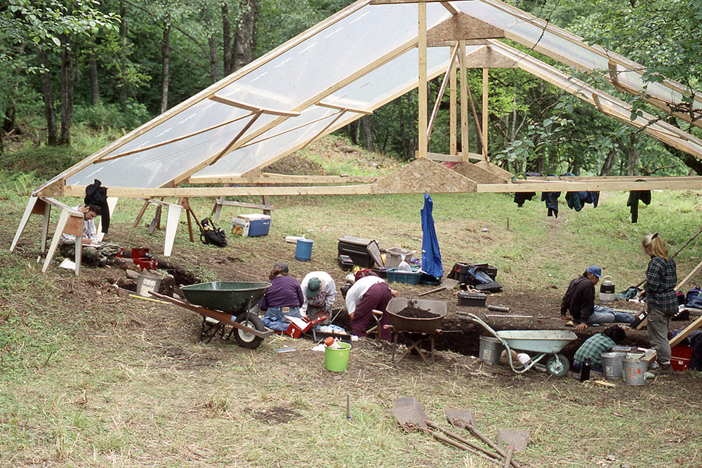 Plusieurs personnes fouillent des sections de terre sous un abri.