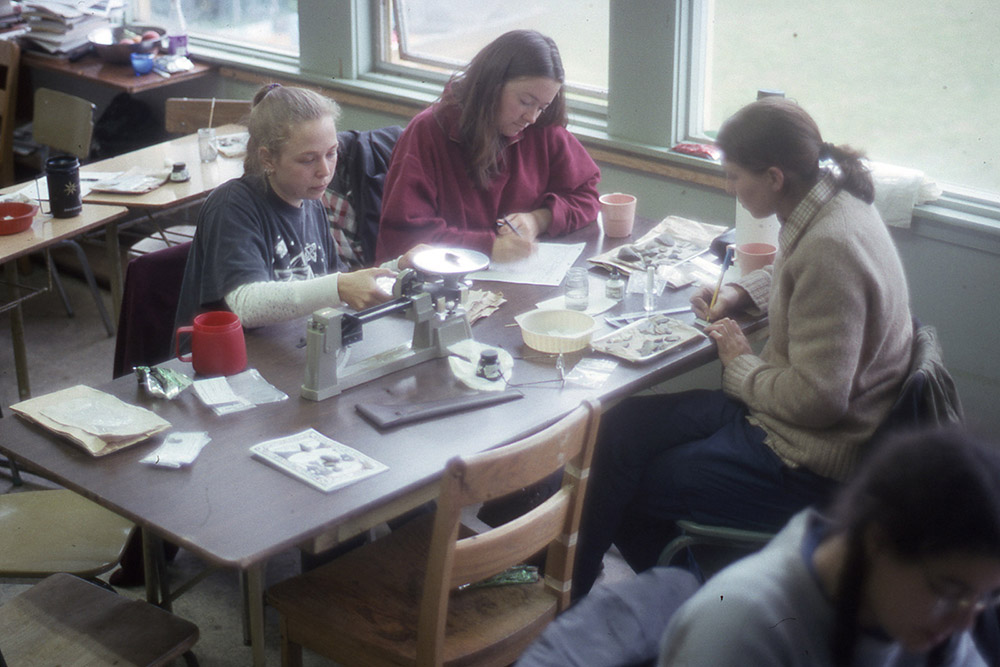 Three students sit around a table, doing lab work.