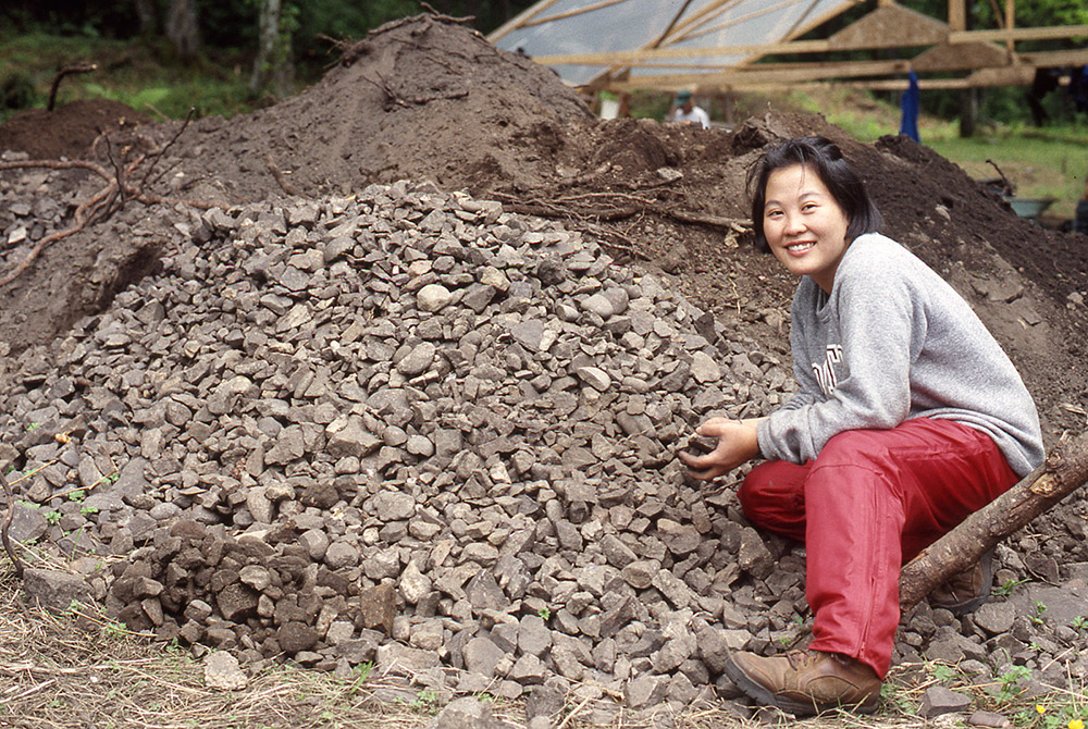 A woman sits beside a large pile of rocks, holding some in her hands.