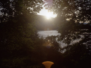 A view of the sun setting over a river with greenery framing the picture.