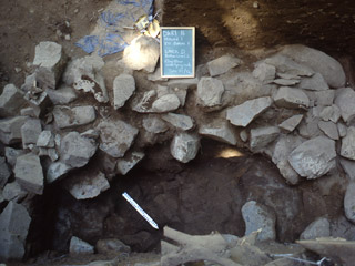 A chalkboard and ruler are placed beside a pile of large rocks inside an excavated mound.