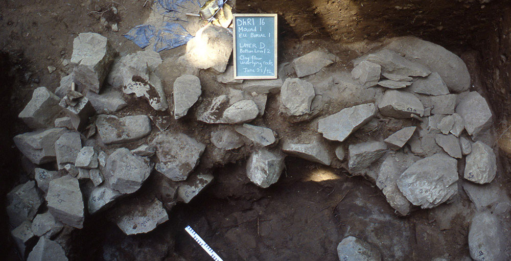 A chalkboard and ruler are placed beside a pile of large rocks inside an excavated mound.