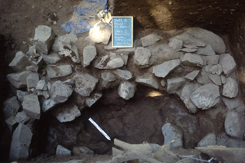 A chalkboard and ruler are placed beside a pile of large rocks inside an excavated mound.