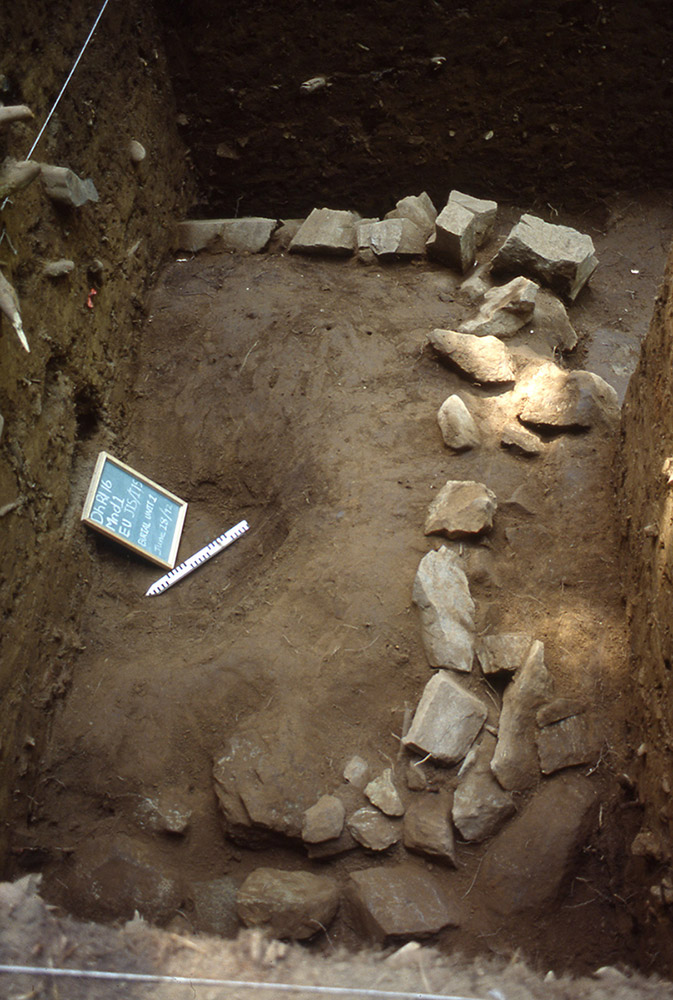 In a section of earth, a chalkboard and ruler are placed beside a square shaped pile of large rocks.