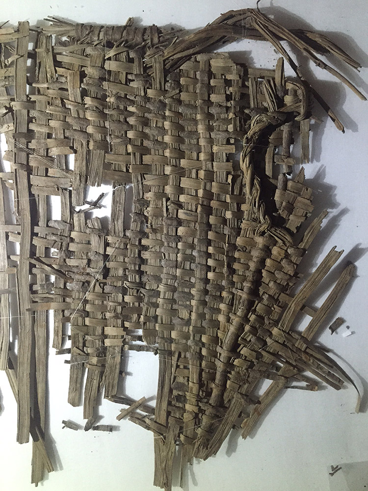 A fragmented basket woven from bark strips. Parts of the rim, body, and handle of the basket are still preserved. 