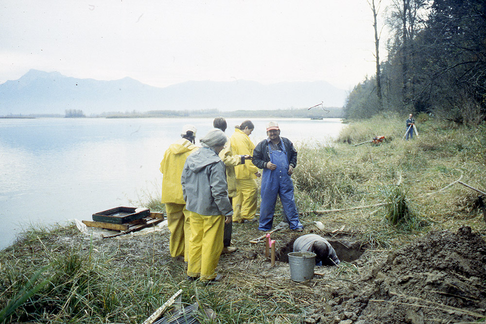 Plusieurs personnes regardent une autre personne creuser une section de terre sur le rivage.