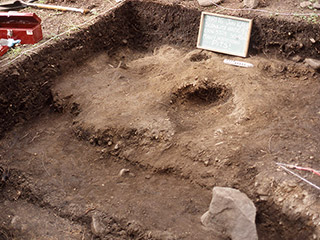 An open archaeological excavation with a hole exposed in the dirt.