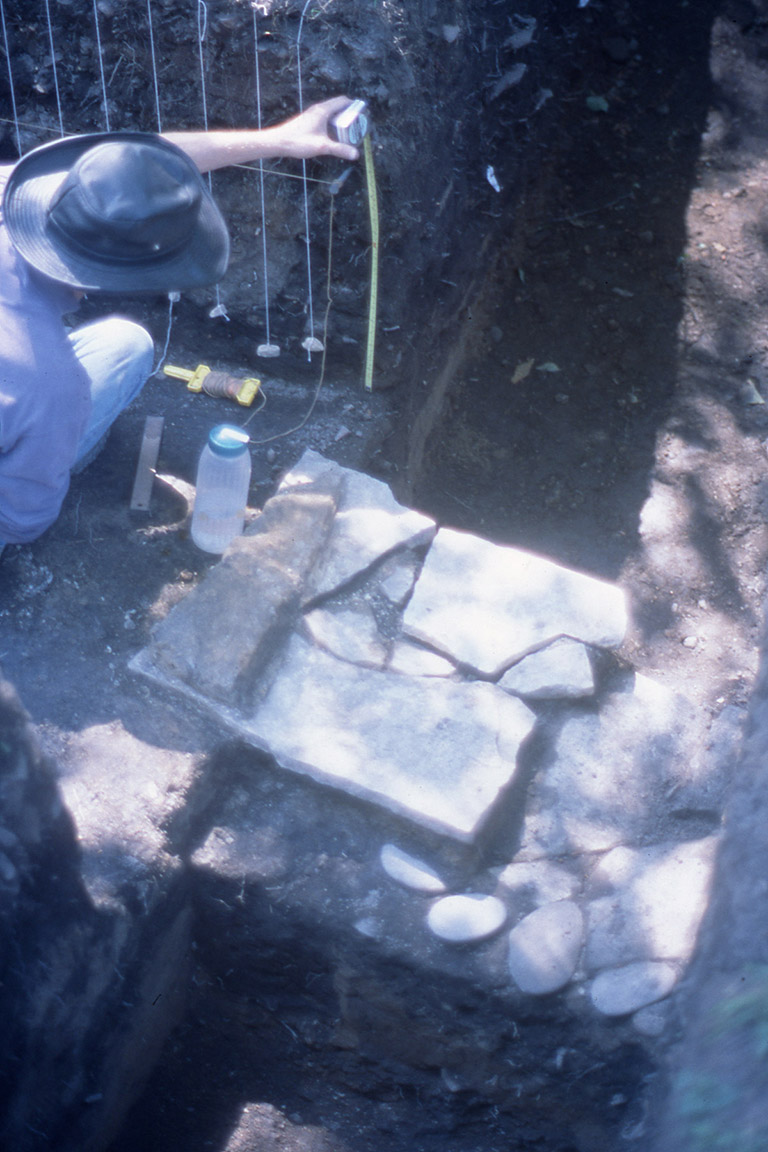 A person kneeling next to flat-fitted square stones, taking measurements.