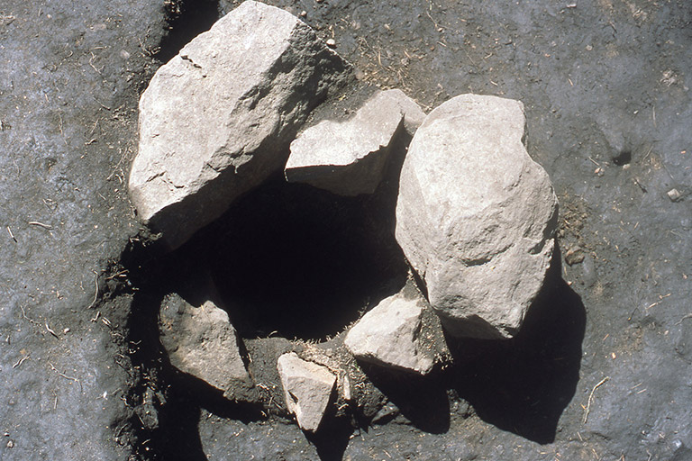Six light grey irregularly shaped boulders, lining a hole in the ground.
