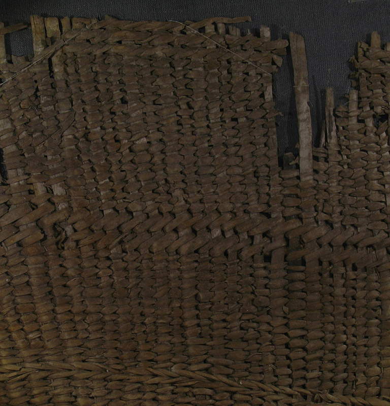 A fragment of woven basketry. The weaving material is brownish red.