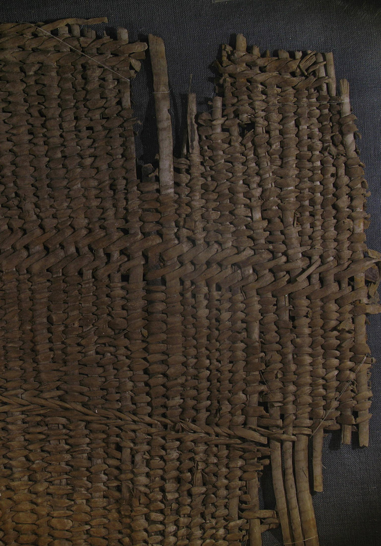 A fragment of woven basketry. The weaving material is brownish red.