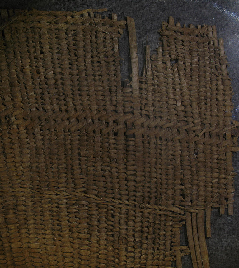 A fragment of woven basketry. The weaving material is brownish red.