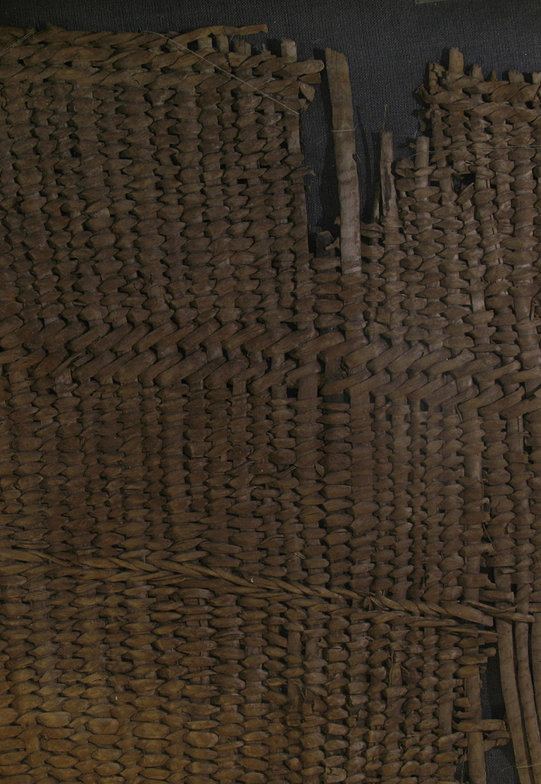 Un fragment de vannerie tressée. Le matériau utilisé pour le tissage est rouge tirant sur le brun.