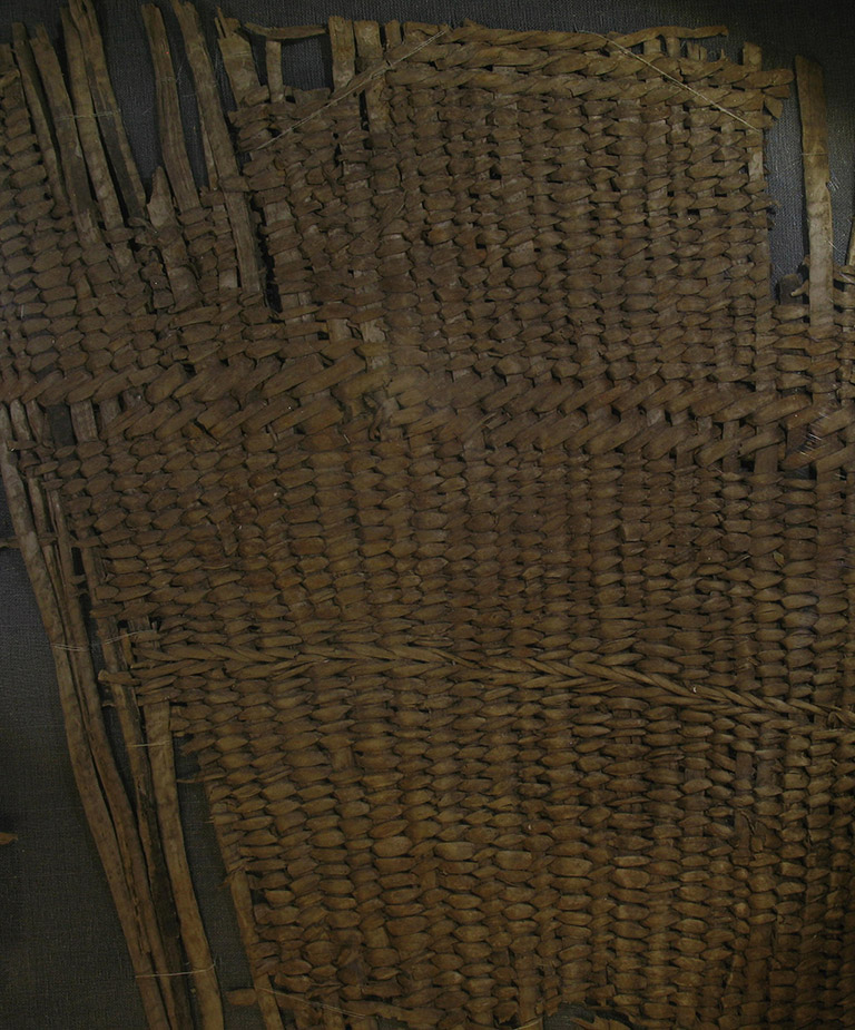 A fragment of woven basketry. The weaving material is brownish red.