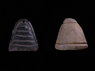 Two small small stone pieces carved into a triangular shape.The black one has an engraved outline and five horizontal lines, and is pierced. The light one has lines etched at the top and bottom.