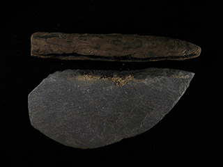 Une pierre gris foncé façonnée en demi-cercle aiguisé, avec un manche de bois qui en est détaché.