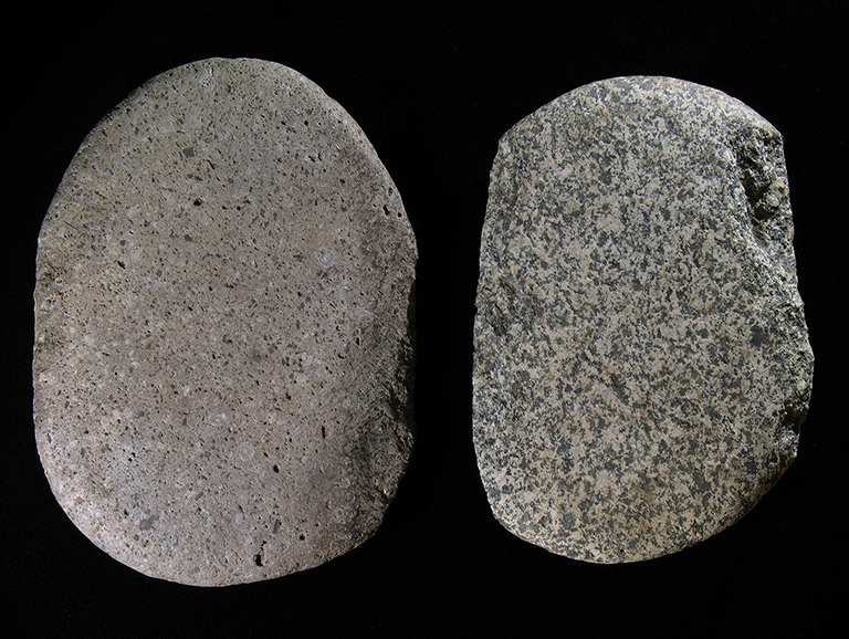 Two large grey stones, the left one smooth and the right one pitted along the edges, are sitting on a black background.