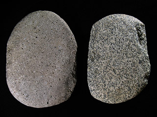 Deux grosses pierres grises; celle de gauche est lisse et celle de droite est trouée sur le bord. Les pierres sont posées sur un fond noir.