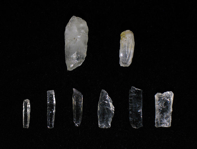 Eight thin pieces of translucent rock are shaped into flat blades. They are varying shades of black to grey.