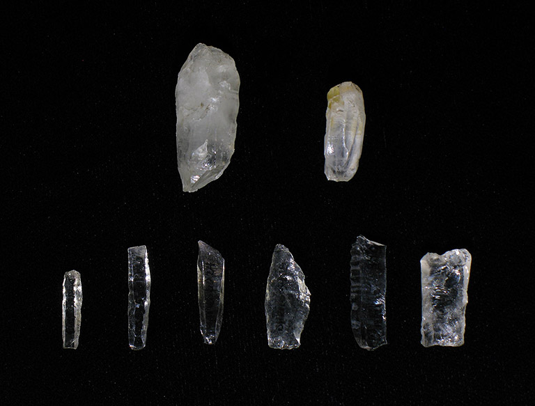 Eight small pieces of translucent light-coloured rock are laying on a black background. Many are shaped into small blades.