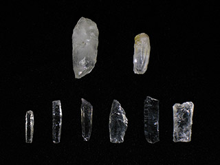 Eight small pieces of translucent light-coloured rock are laying on a black background. Many are shaped into small blades.