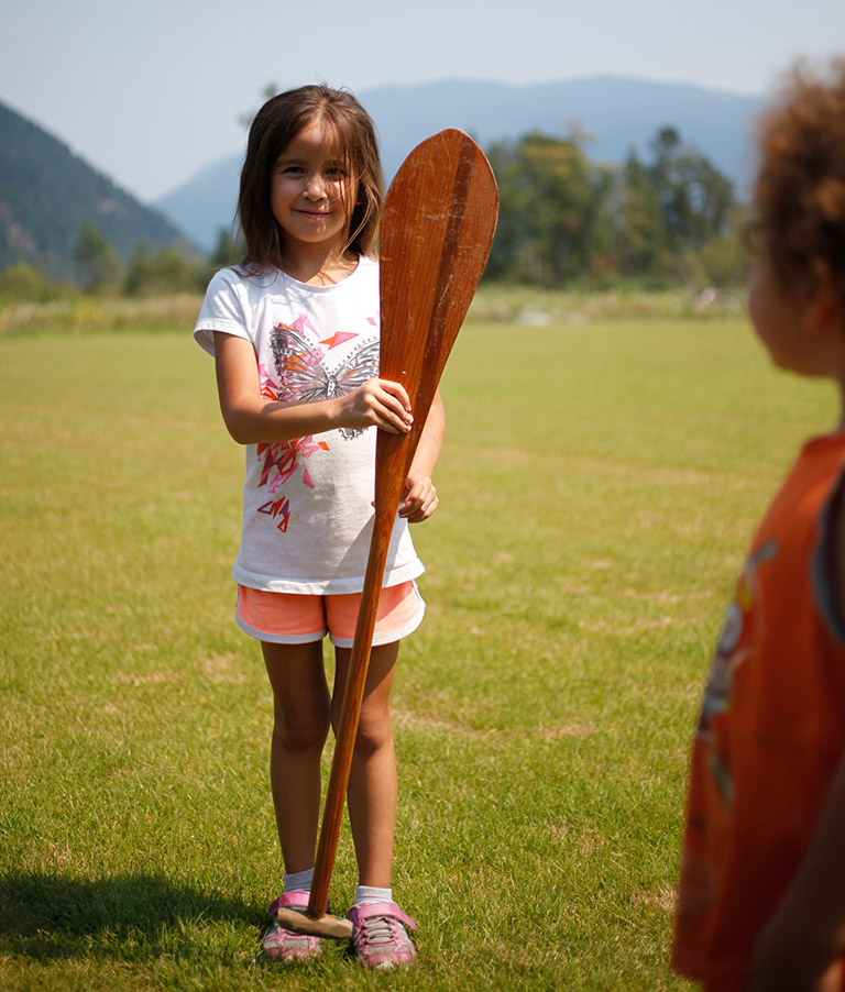 Young girl holding a paddle that is as tall as her.