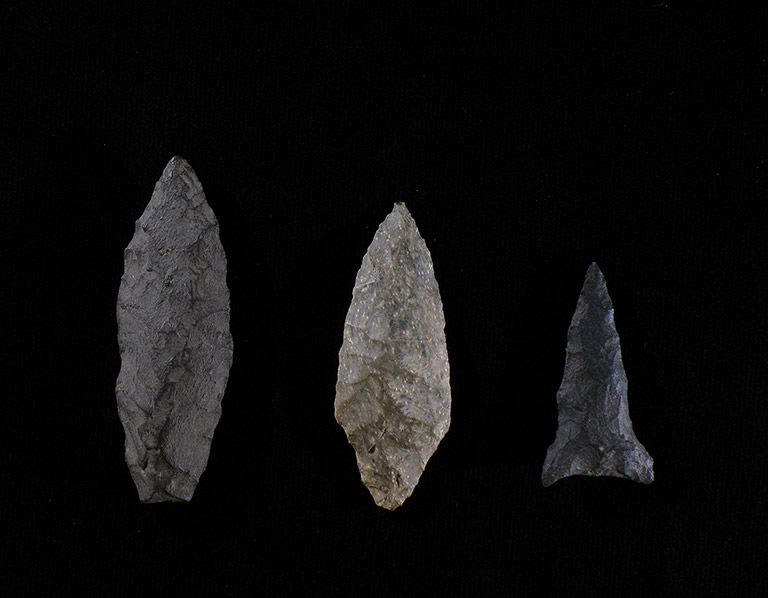 Three arrowheads of different sizes, in various shades of grey, on a black background.