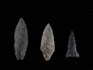 Three arrowheads of different sizes, in various shades of grey, on a black background.