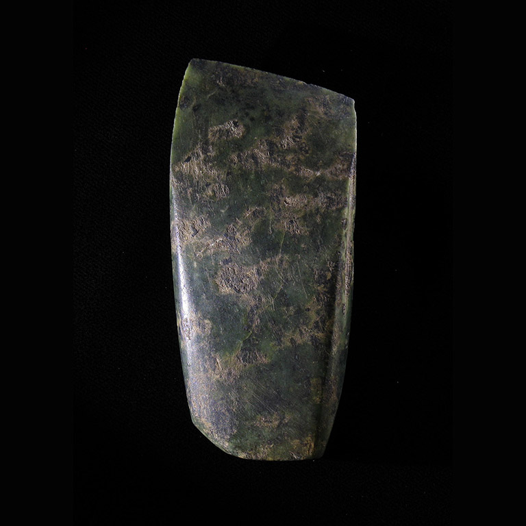 Une pierre vert foncé en forme de rectangle avec un bord aiguisé.