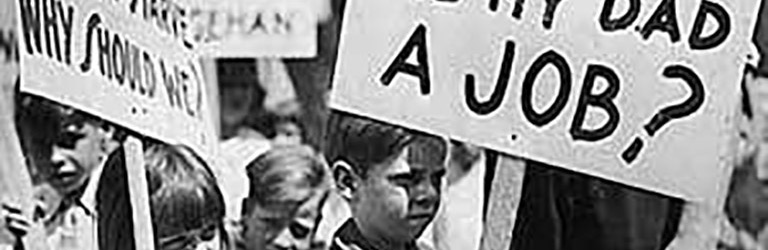 Des enfants tiennent des pancartes lors d’un rallye. Sur les pancartes, il est écrit « Why can’t you give my dad a job? » (Pourquoi ne pouvez-vous pas donner du travail à mon papa?) et « Rarig’s kid doesn’t starve why should we? » (L’enfant de Rarig n’a pas faim, pourquoi devrions-nous avoir faim?)