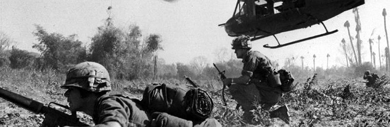 Soldiers lying flat on the ground with a helicopter above them