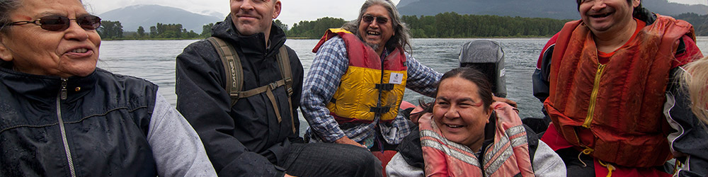 Five people are seated inside a small motorized boat, travelling across the river. 