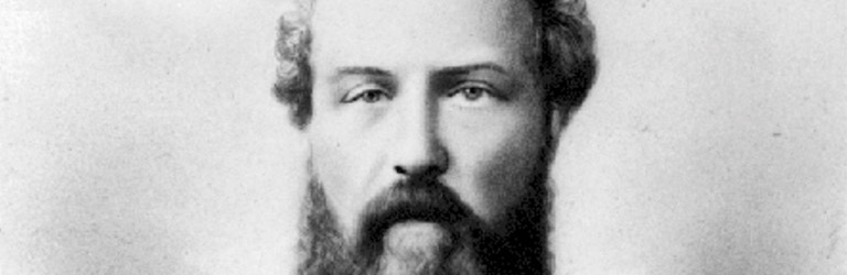 Une photo en noir en blanc d’un homme avec une longue barbe et une moustache tombante.