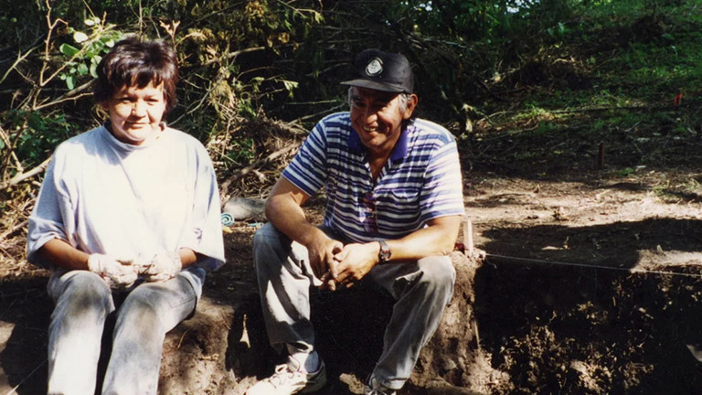 A man and woman sit side-by-side on the ground.