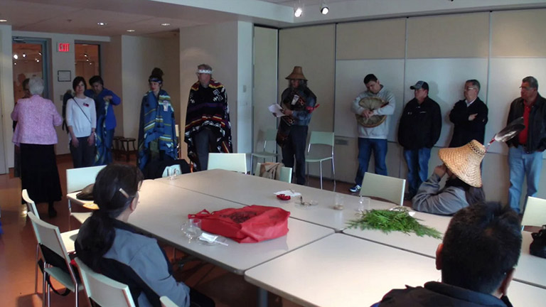 Un groupe d’aînés et d’adultes debout autour d’une table sur laquelle il y a des branches de cèdre.