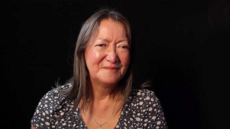 A woman elder smiles for a photograph while she shares a story.