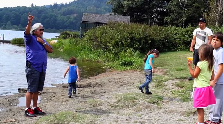 Un groupe d’enfants près de la rive écoutent un aîné raconter des histoires.