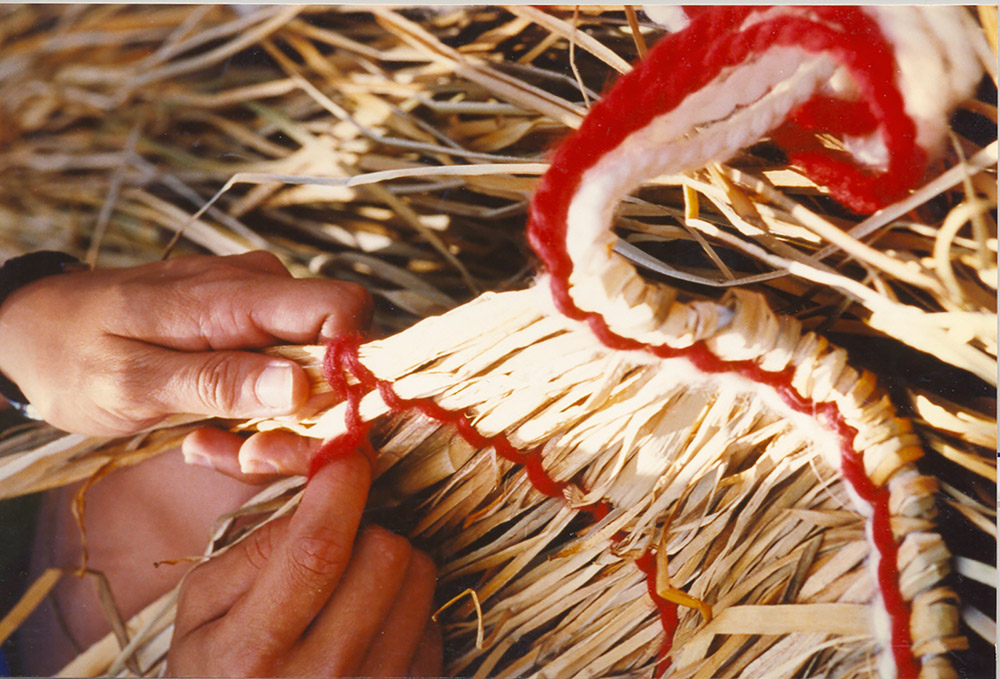 A woman ties cattails to make a traditional skirt.
