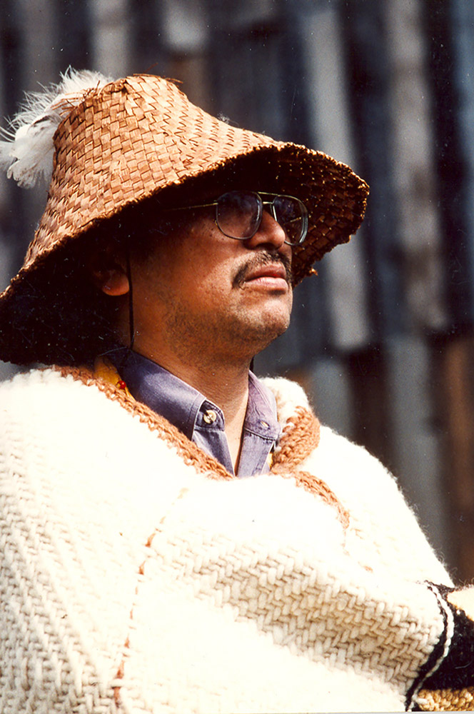A photograph of a man wearing a woven hat and blanket.