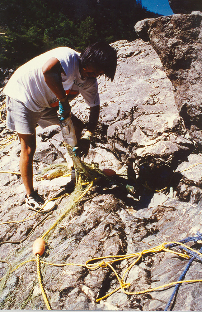 Un homme sur une rive rocailleuse démêle un filet pour en sortir un poisson.
