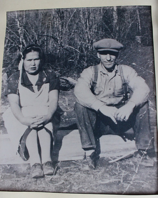 A black and white photograph of a young couple sitting side-by-side on a blanket on the grass outside.