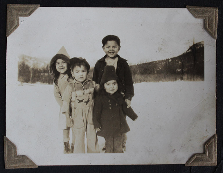 Une photo en noir et blanc de deux fillettes et deux petits garçons debout dans un champ enneigé. Ils portent des vêtements d’hiver.