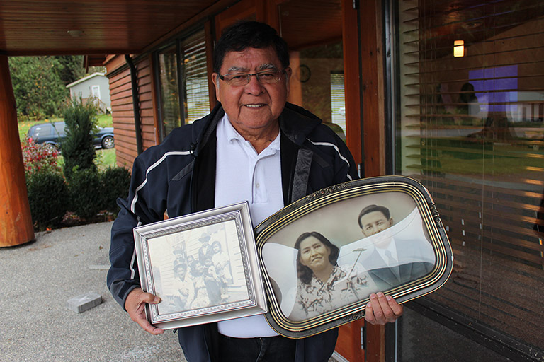 A man stands next to a building with two framed photographs in his hands.