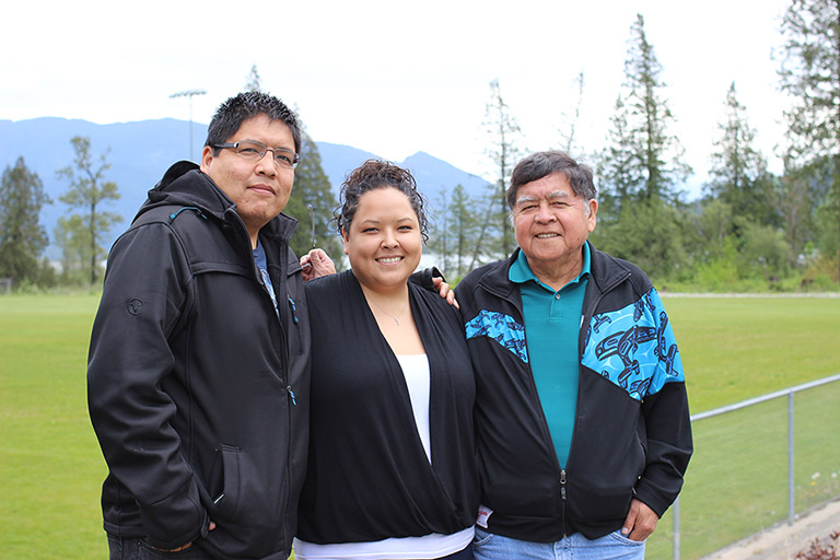 A woman stands between two men in front of a soccer field with their arms around each other. The man on the right is the father.